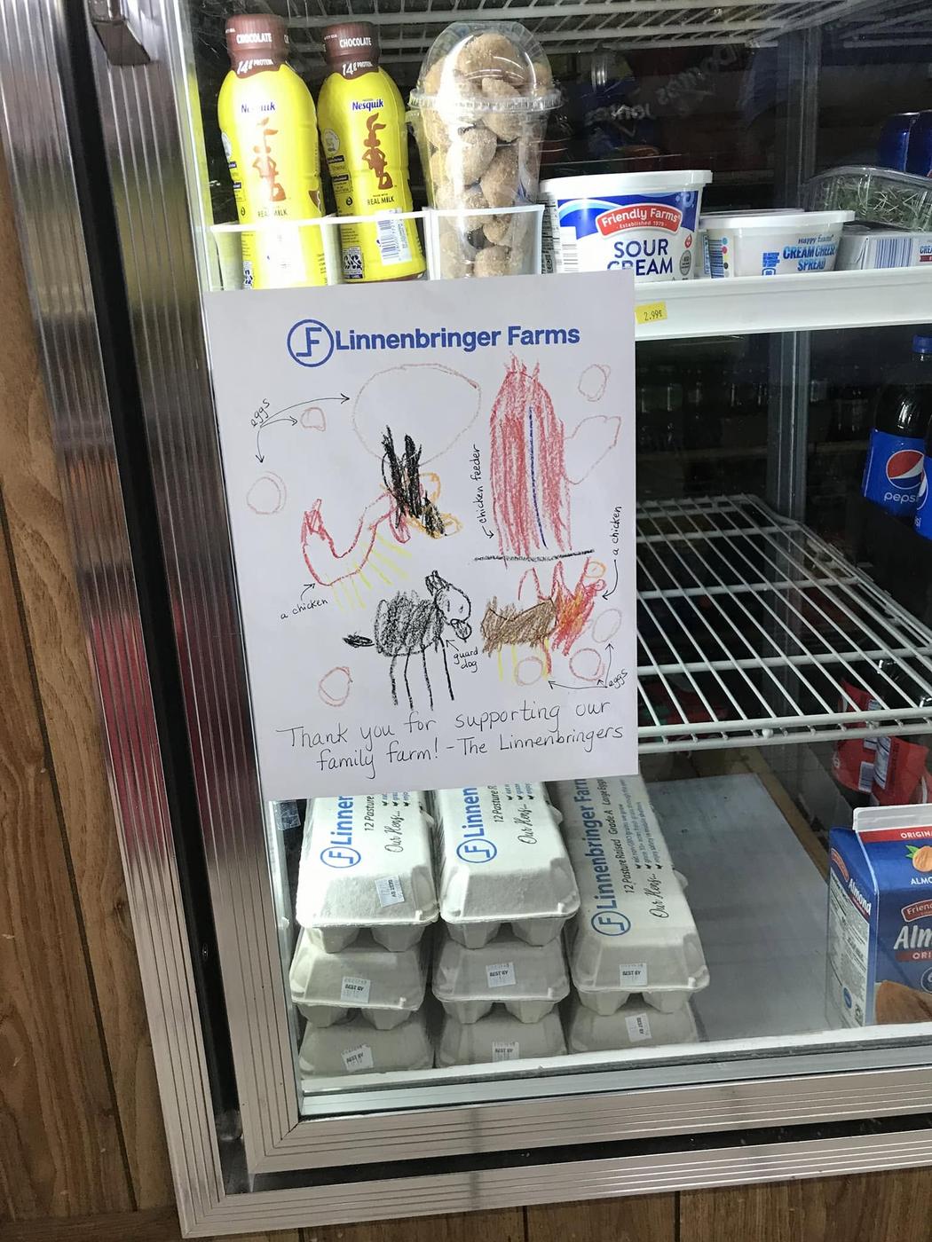 The egg fridge at Shaw Market stocked with Linnenbringer Farms eggs, with a child's crayon drawing taped up thanking the store for supporting their family farm