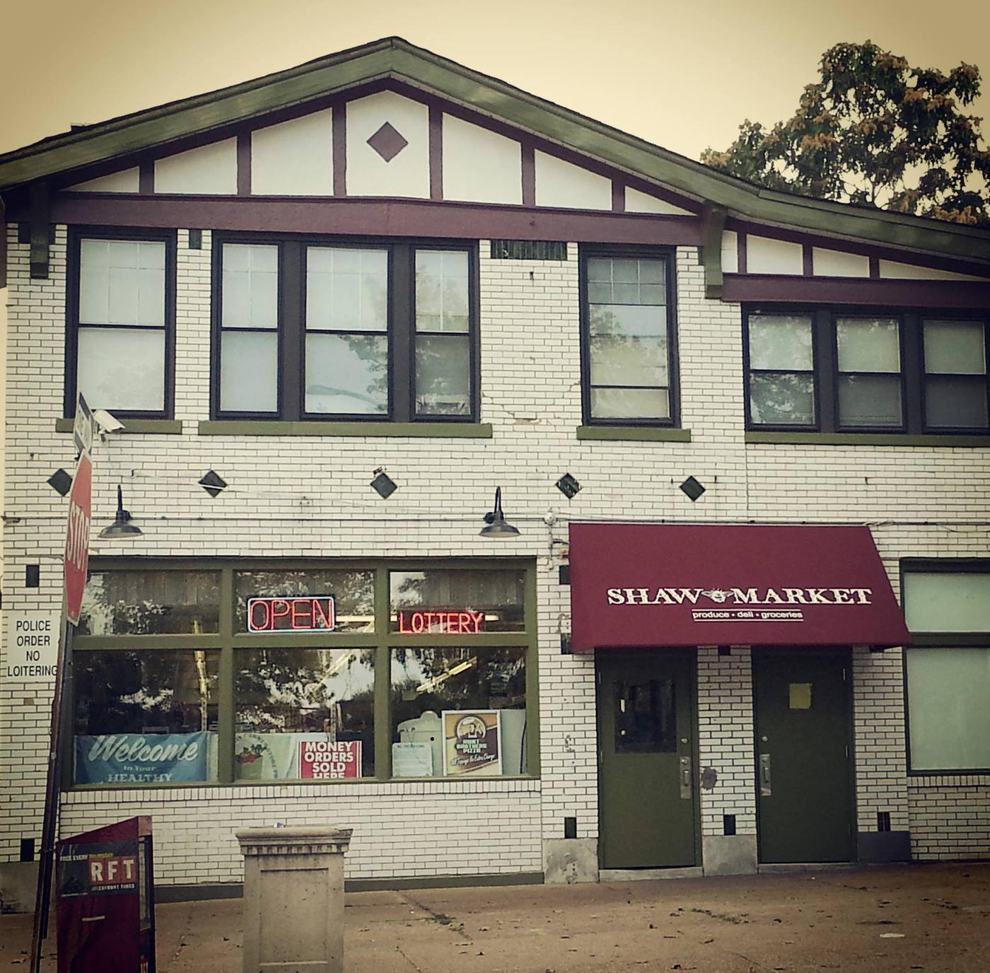 The Shaw Market storefront: white painted brick under a Tudor gable, with a deep red awning reading SHAW MARKET, produce, deli, groceries